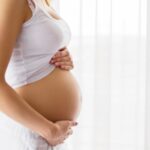 Une femme enceinte souriante se tenant le ventre avec tendresse.